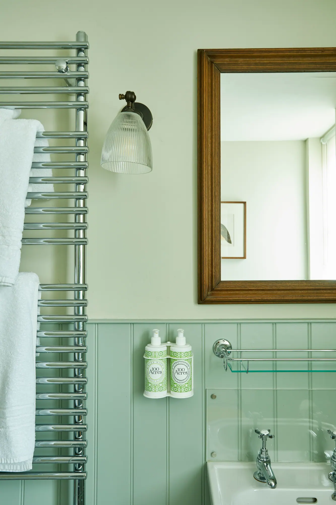 A mint-green panelled bathroom with a heated towel rail and 100 Acre Apothecary toiletries