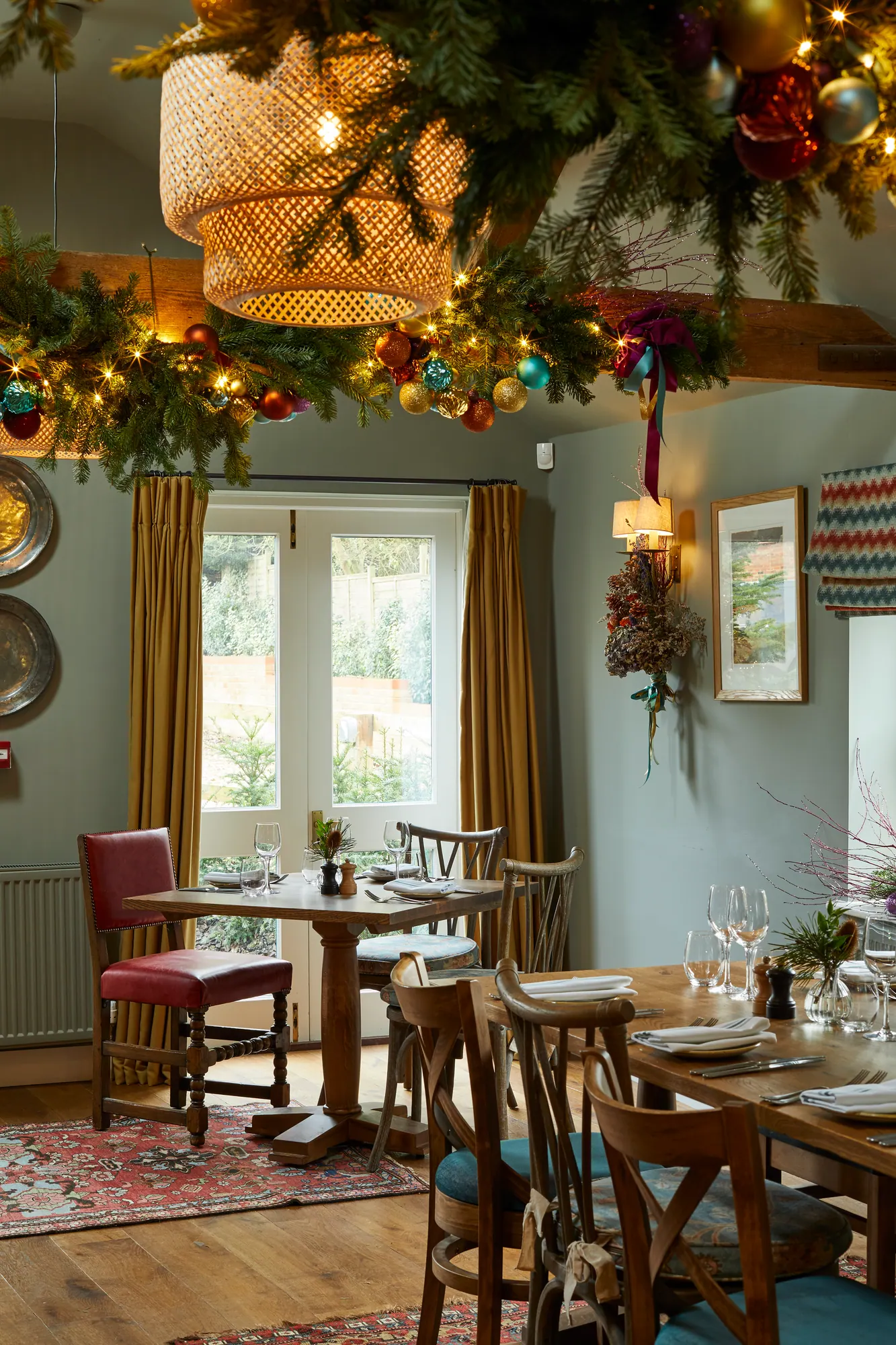 Christmas garlands and a woven lampshade above tables laid for festive lunch