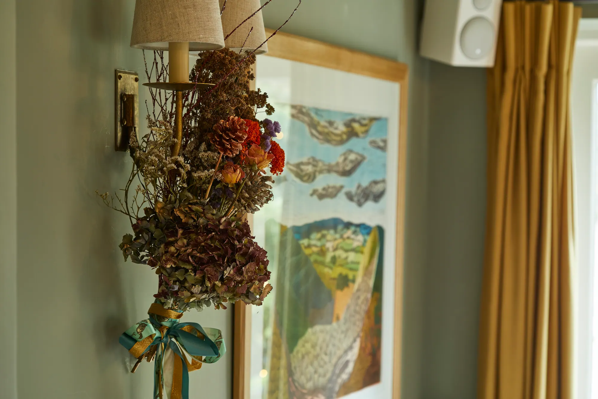 A posy of dried flowers tied with ribbon, hung beside a painting of the downs