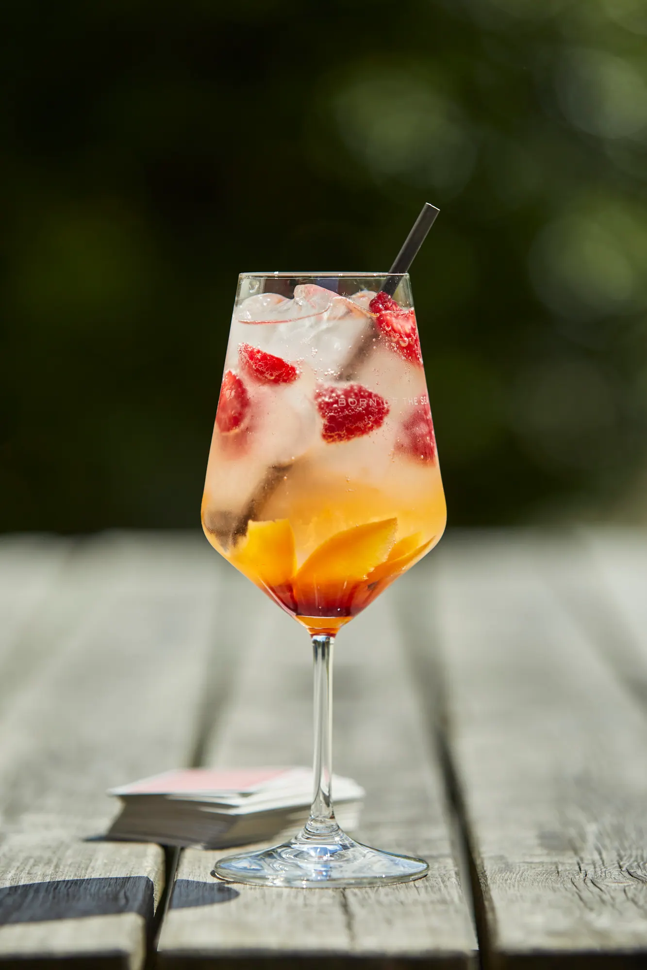 A spritz with raspberries and a slice of orange in a stemmed glass, on a weathered table outside