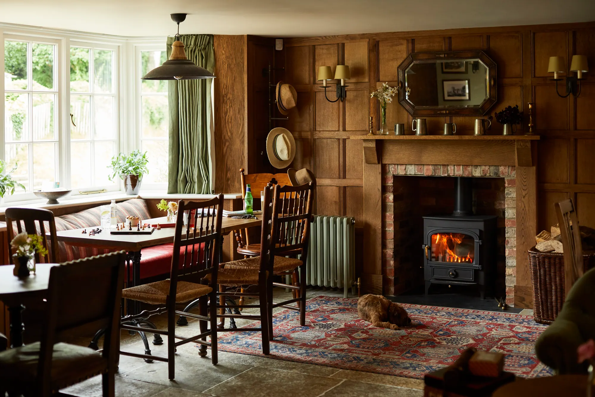 The oak-panelled bar room with a lit log burner, tables laid for lunch and a small dog on the rug