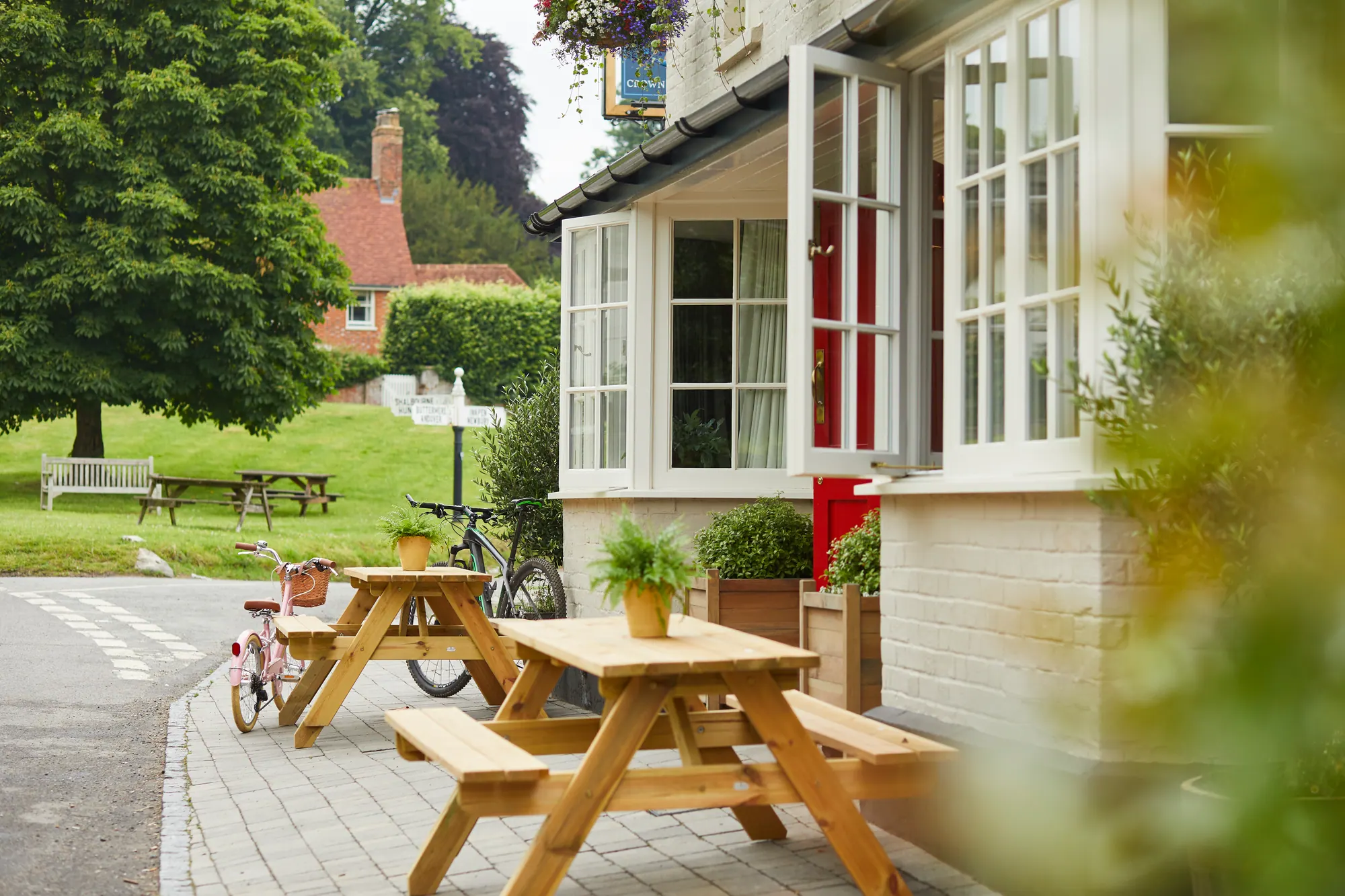 Wooden picnic tables on the front terrace, looking across the lane to the village green, bicycles leant against the wall