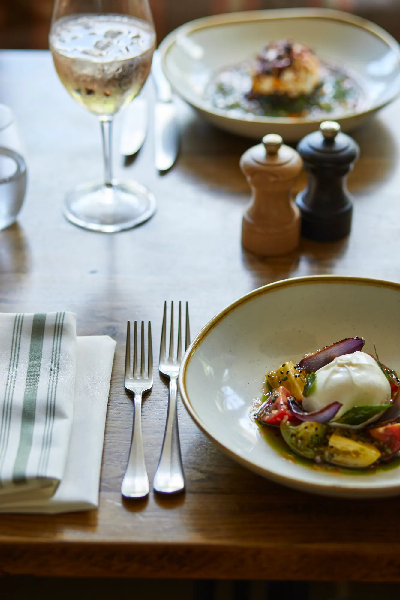 Burrata with heritage tomatoes and red onion, a glass of white wine and a second plate across the table