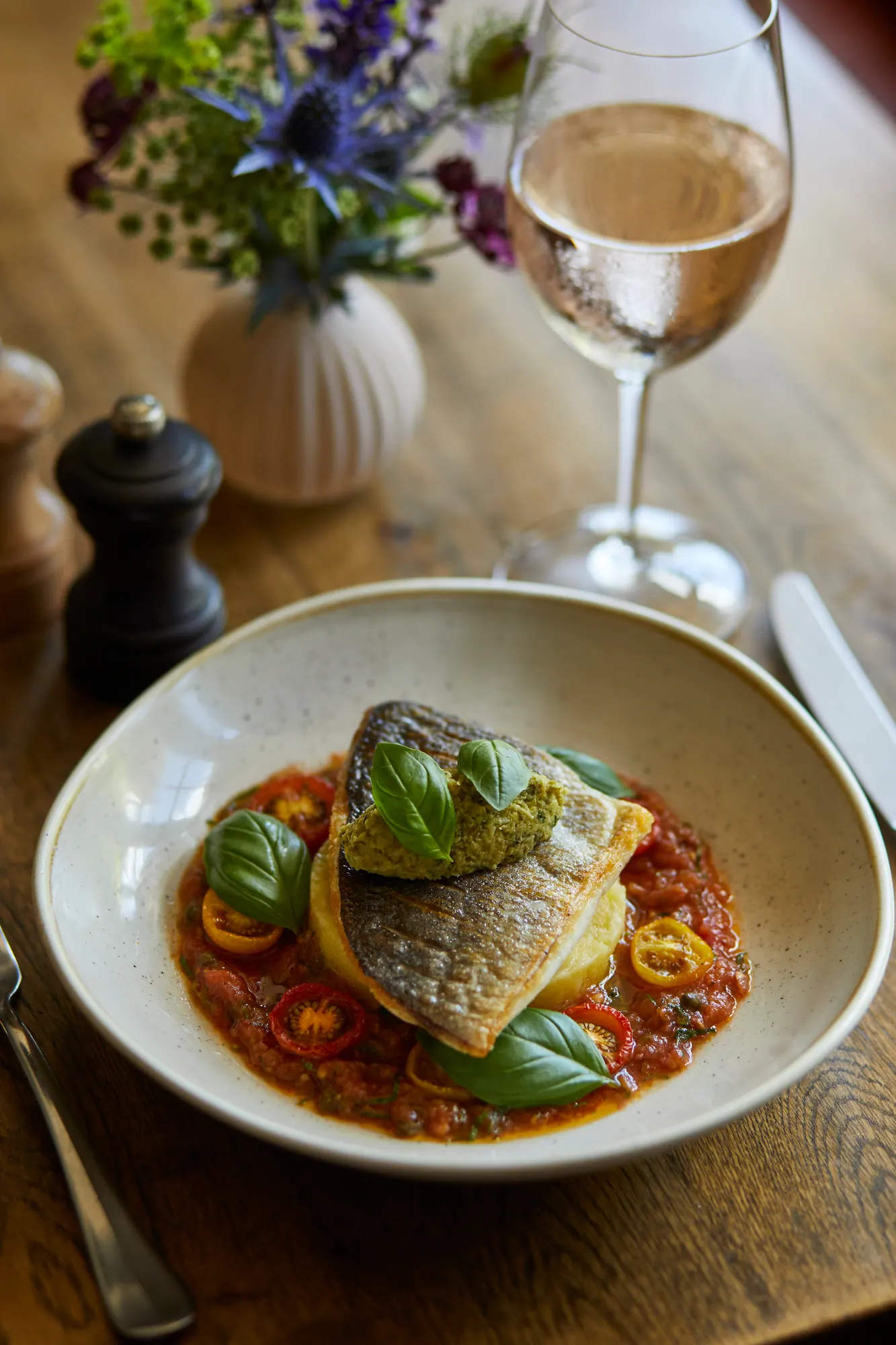 Pan-fried sea bream on a tomato and pepper stew with basil leaves, a glass of rosé behind