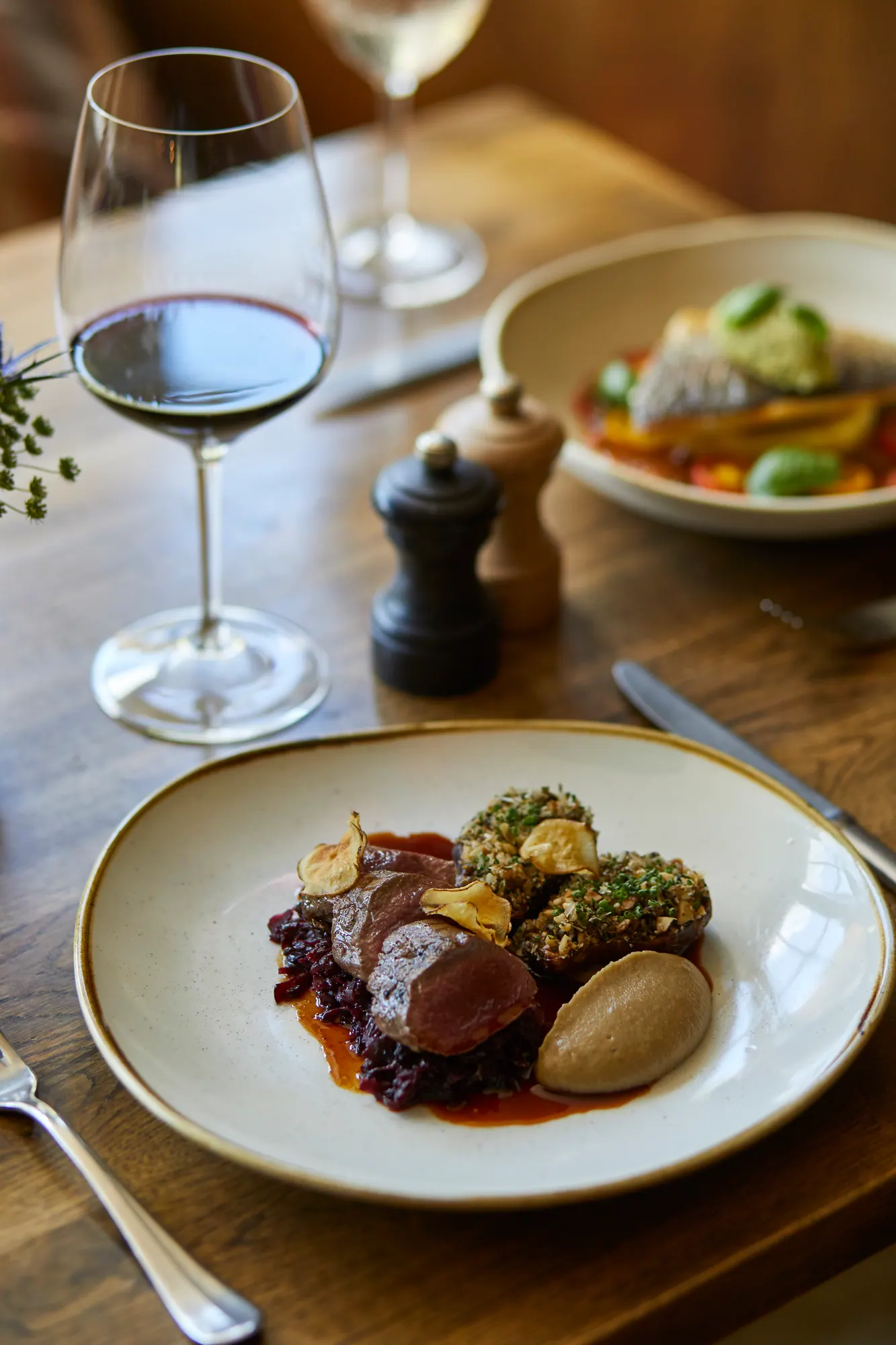 Pink-roasted meat with red cabbage, greens and a potato fondant, with a glass of red wine