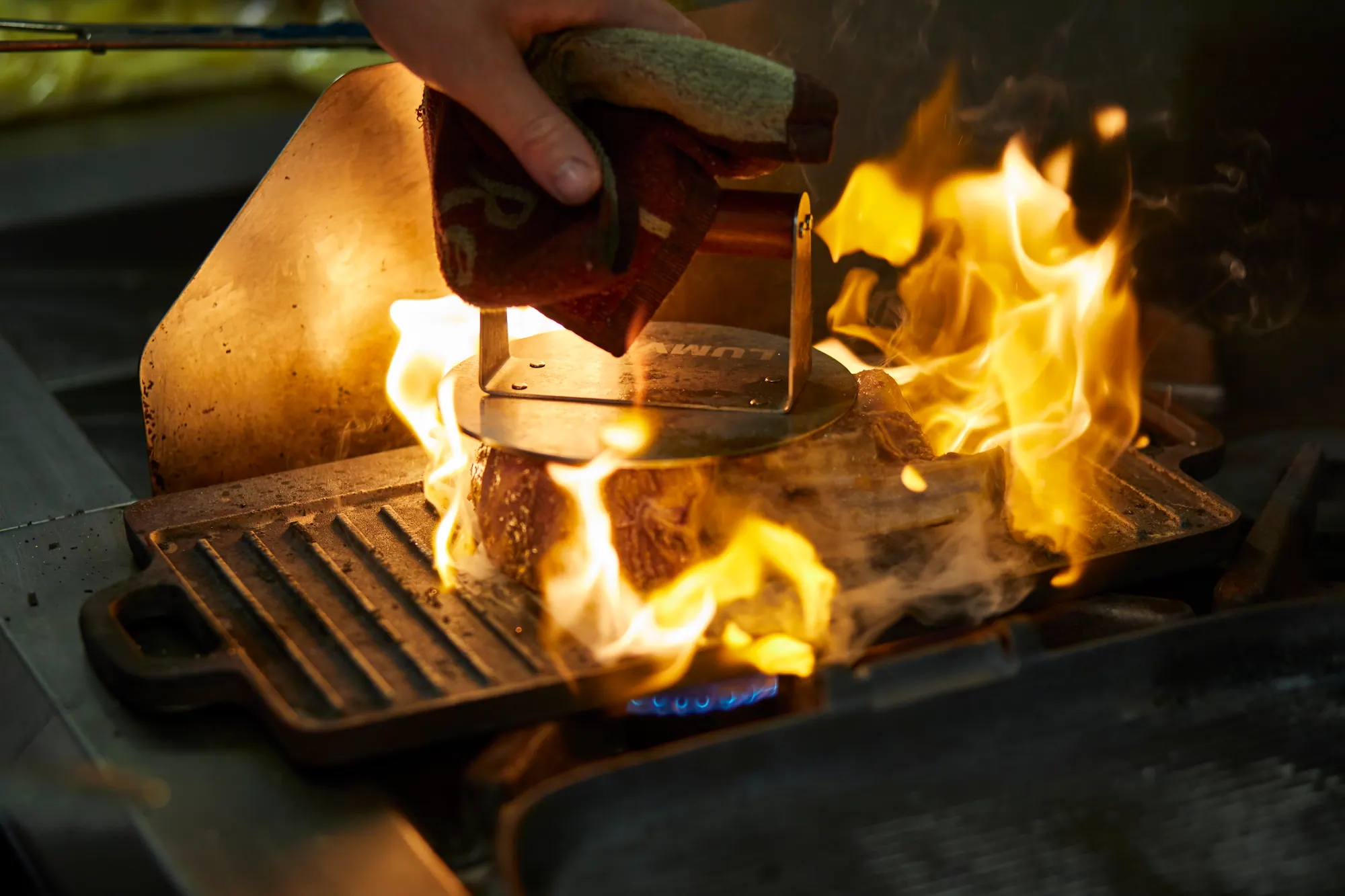 Meat searing over leaping flames on a cast-iron grill in the kitchen