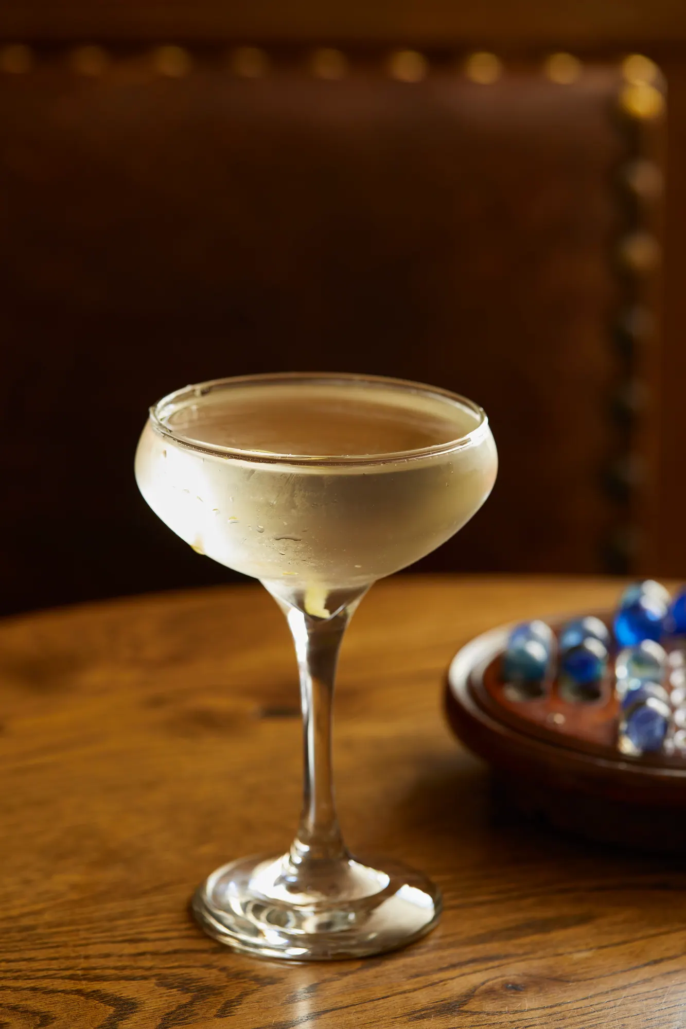 A martini in a coupe glass on a polished wooden table, a marble solitaire board beside it