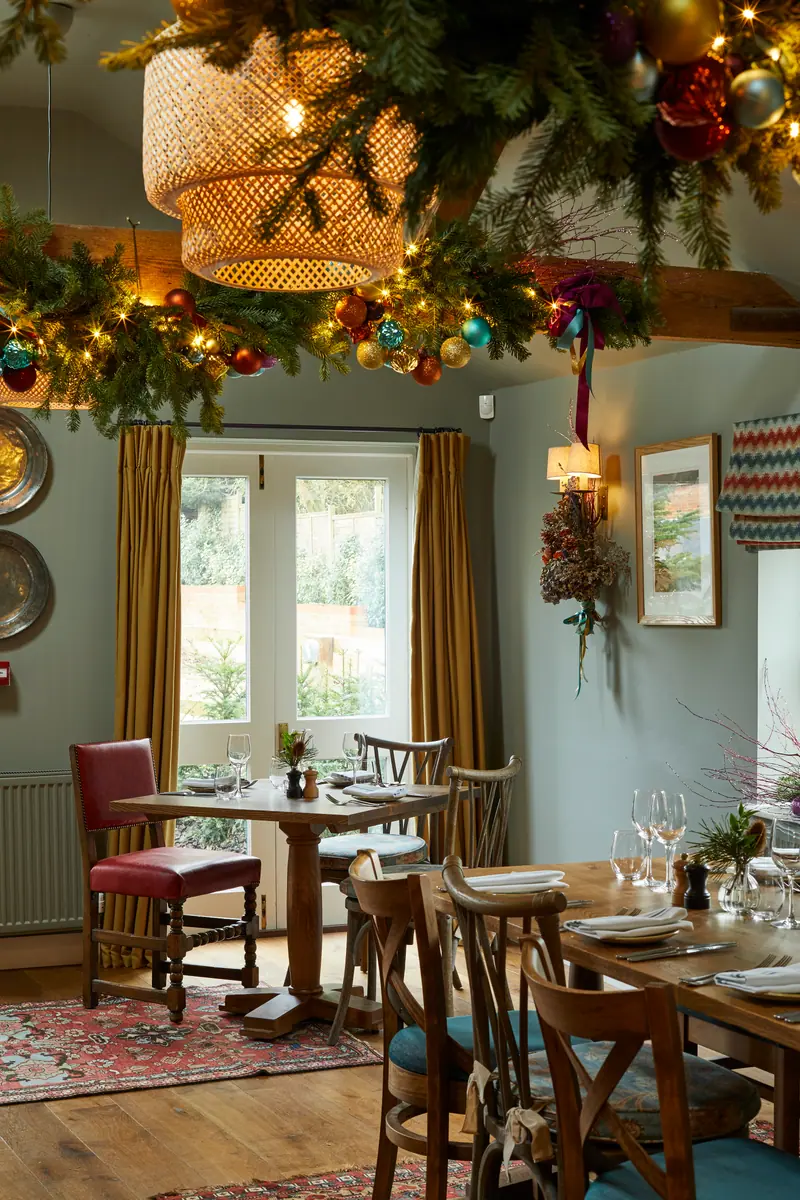 Christmas garlands and a woven lampshade above tables laid for festive lunch