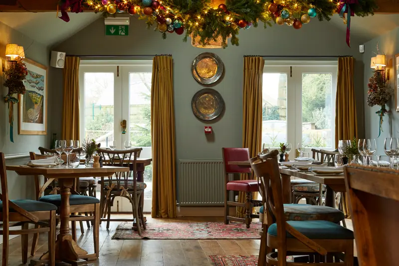 The garden dining room at Christmas, a garland of baubles and greenery strung across the ceiling