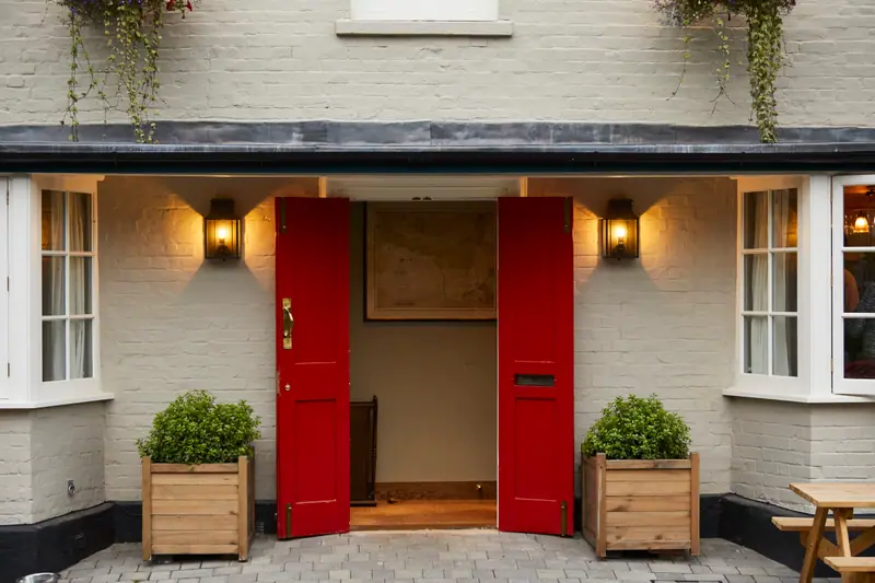 The pub's red double doors thrown open between two box-hedge planters