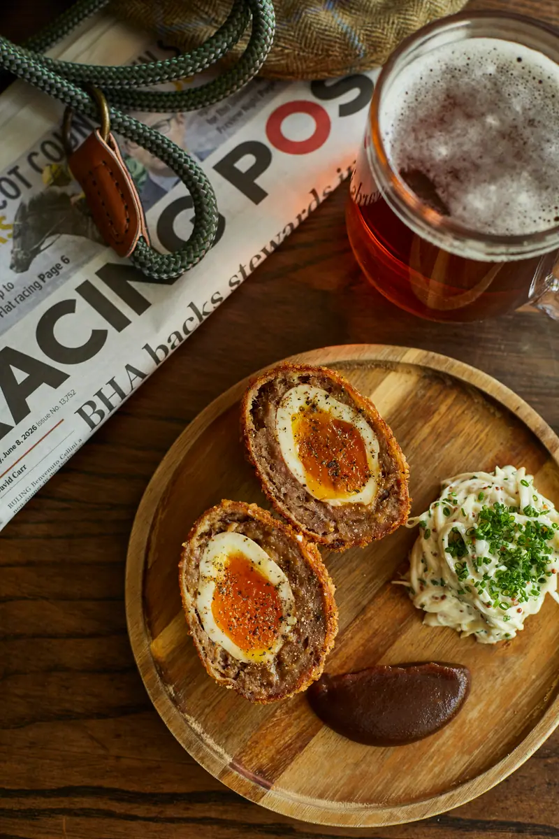 Scotch eggs on a wooden board beside the Racing Post and a pint of ale