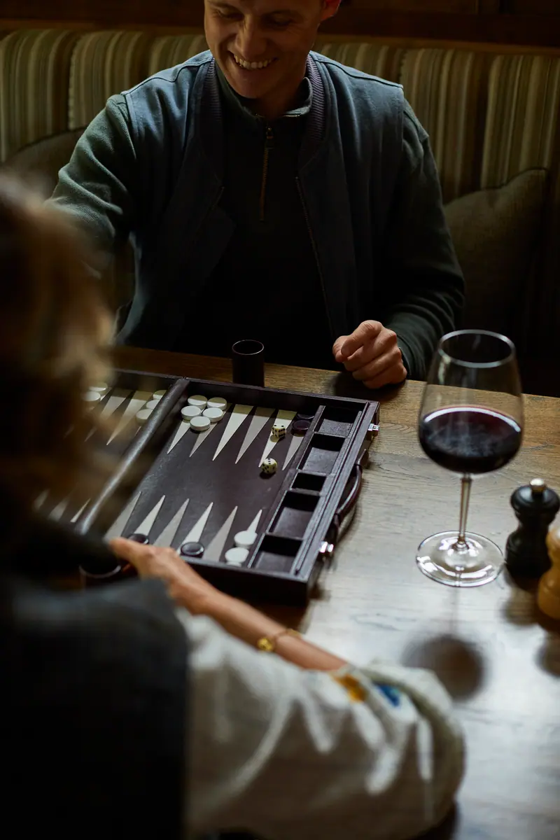 A game of backgammon over a glass of red wine on a cushioned banquette