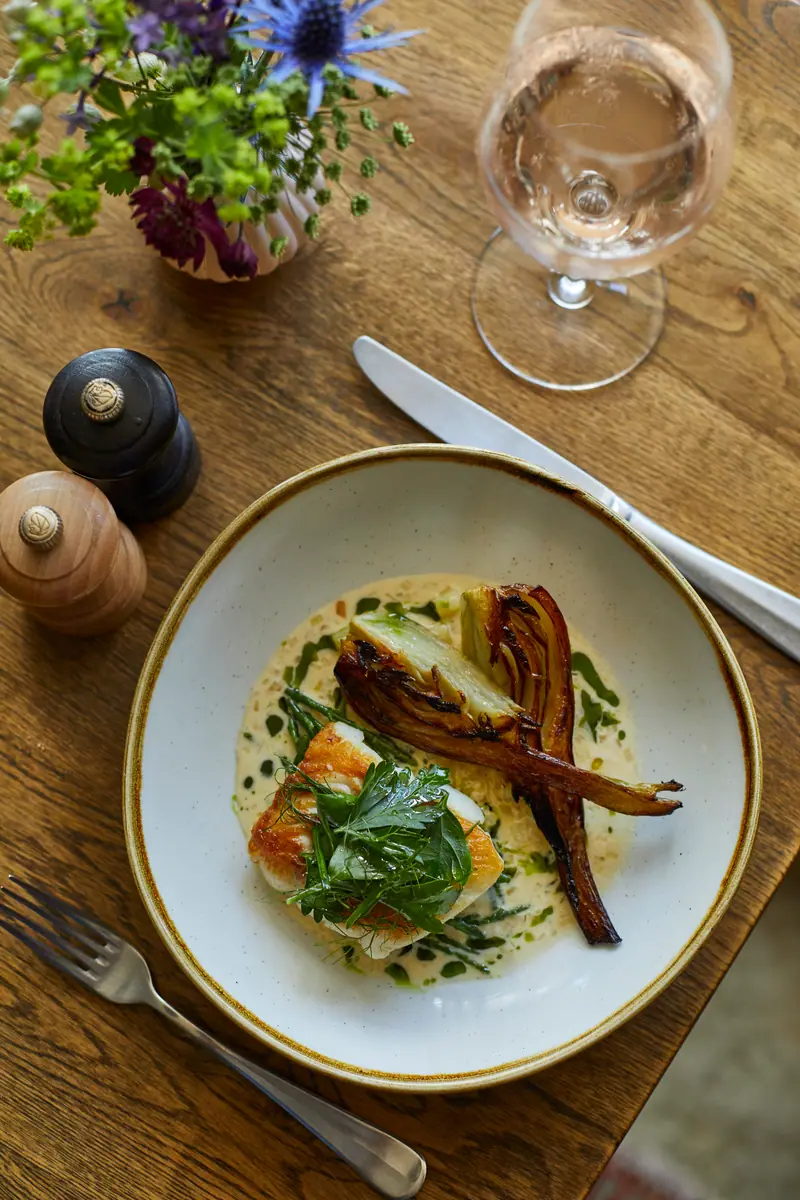 A fillet of white fish with charred vegetables and a butter sauce, a glass of rosé alongside
