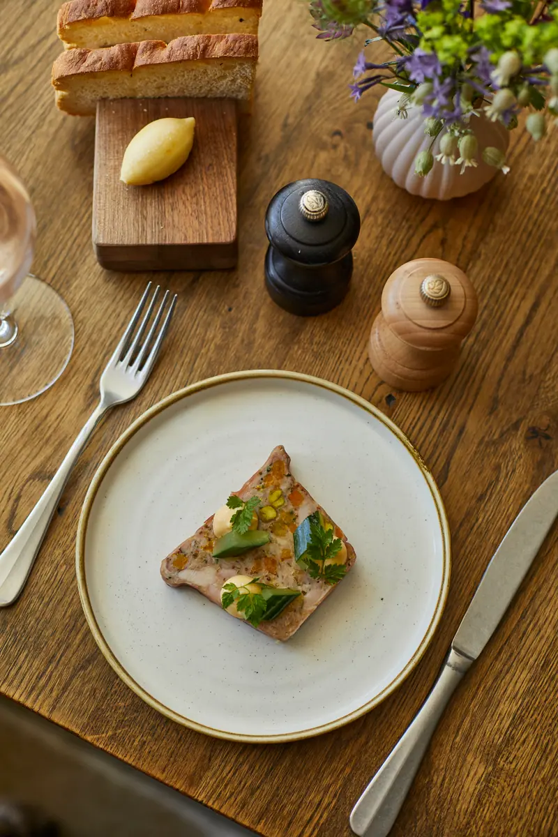 A small starter on toast with herbs, bread and butter on a board and a pepper mill on the oak table