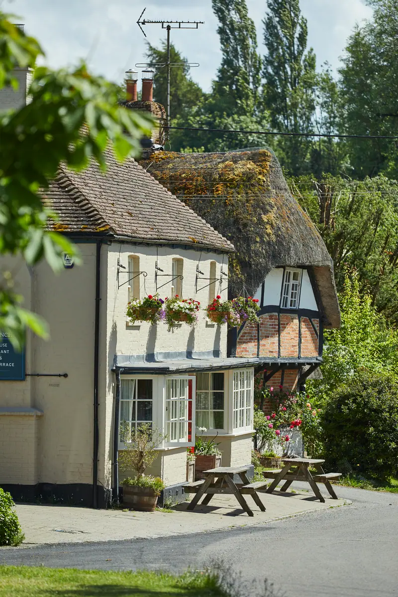 The Crown & Anchor seen from the lane, a thatched cottage beside it and picnic benches out front in the summer sun