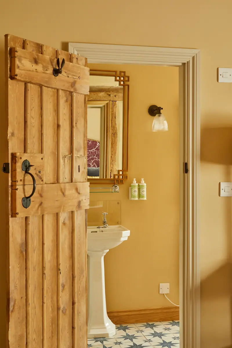 A reclaimed plank door opening onto a warm yellow bathroom with star-patterned floor tiles