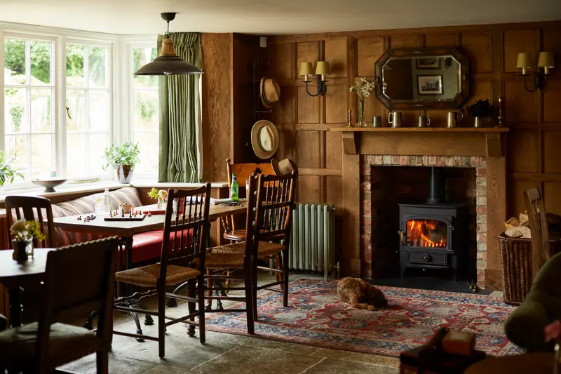 The oak-panelled bar room with a lit log burner, tables laid for lunch and a small dog on the rug