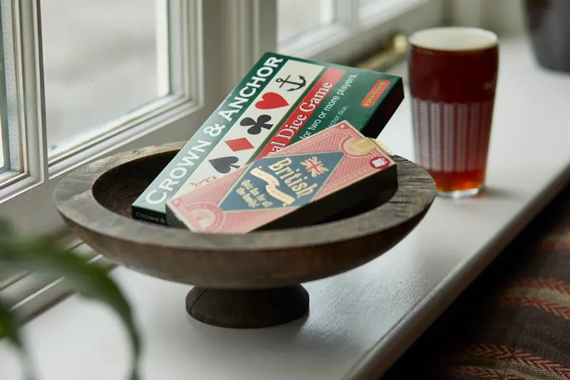 A Crown & Anchor dice game in a wooden bowl on a windowsill, with a pint of ale beside it