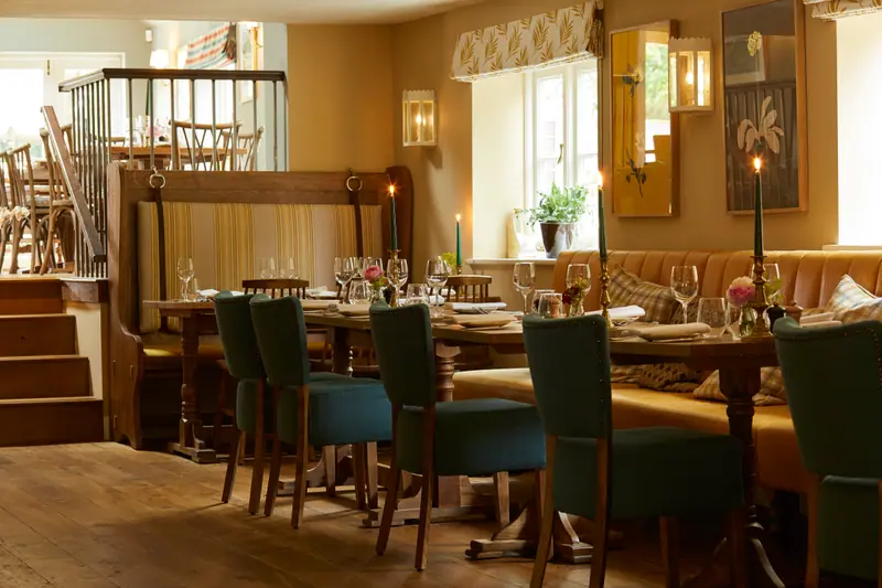 The long dining room, candles lit along tables of green velvet chairs and a striped banquette