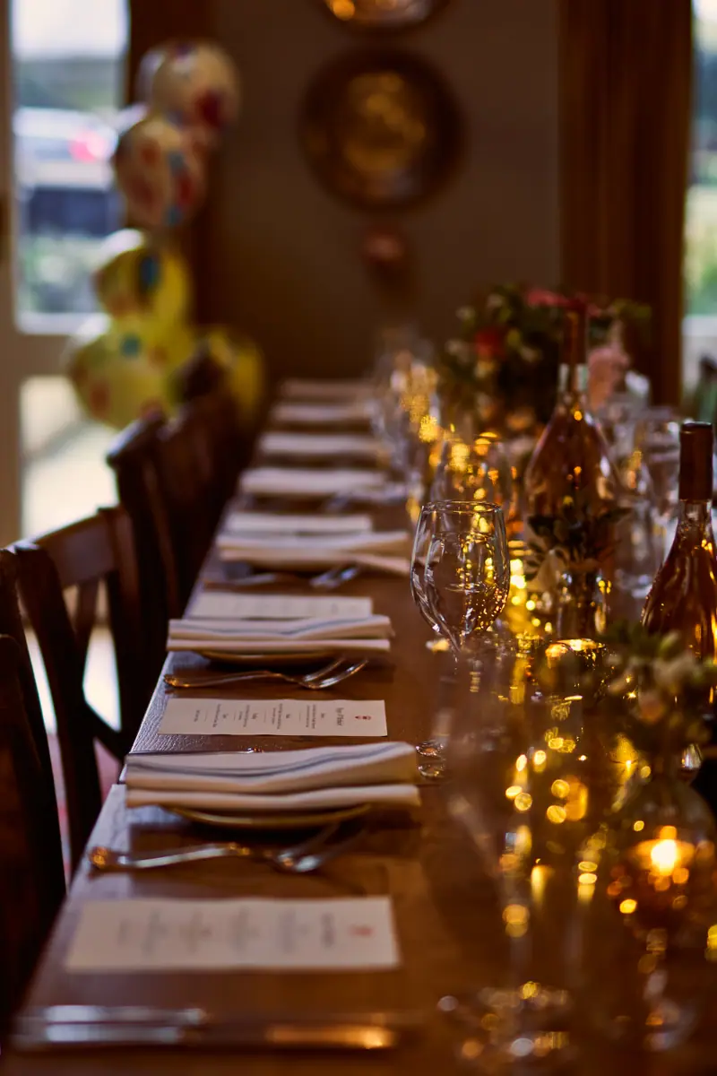 A long table set for a private dinner, glowing with candles, glasses and printed menus