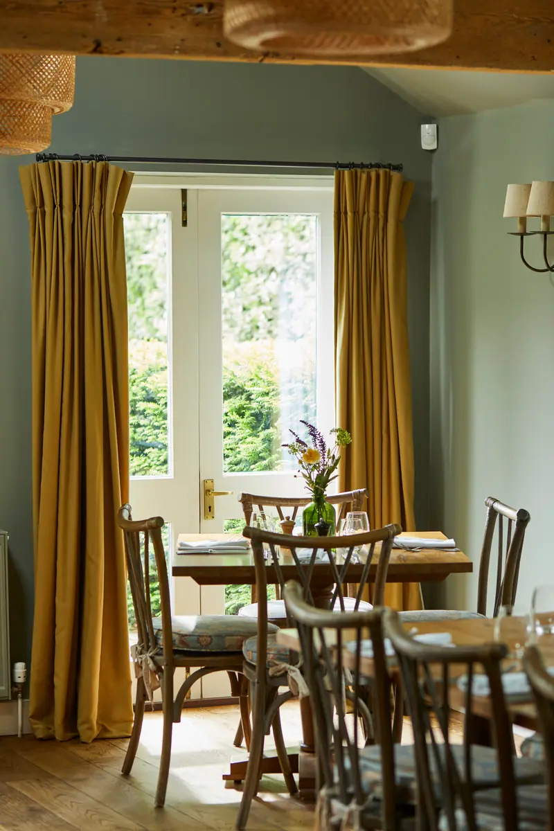 The garden dining room, with mustard curtains framing French doors and tables laid for lunch