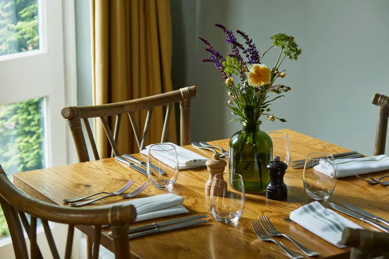 A table laid for dinner with wildflowers in a green glass vase and the garden beyond the window