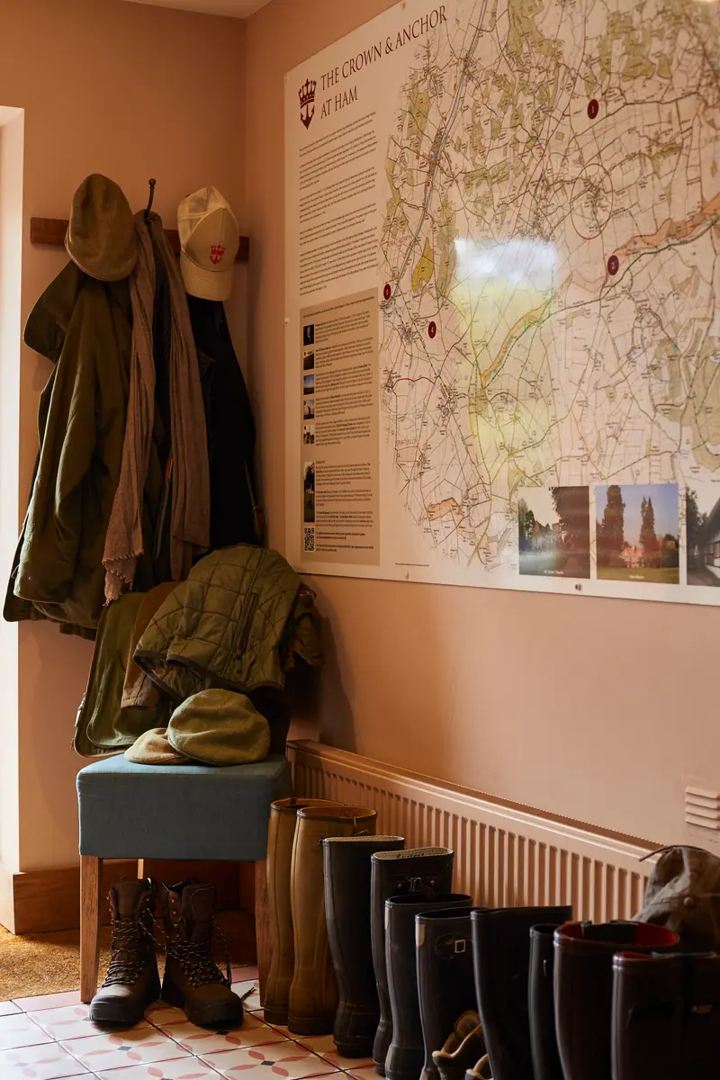 The boot room: waxed coats and hats on pegs, wellies lined up below and a large map of local walks on the wall