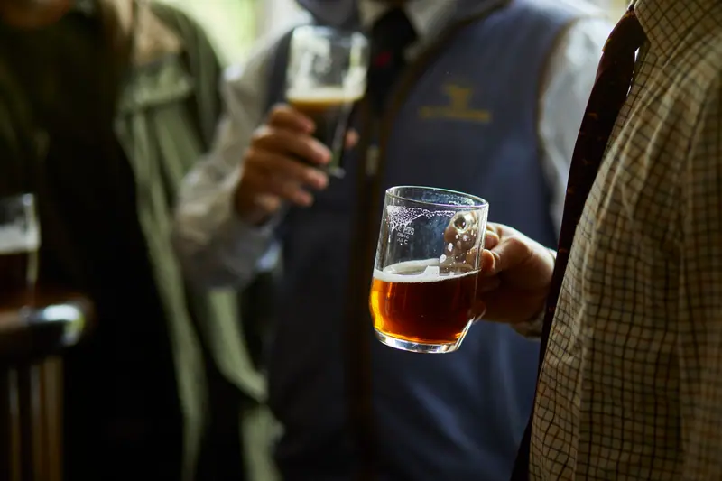Pints of ale raised among friends in tweed and gilets at the bar