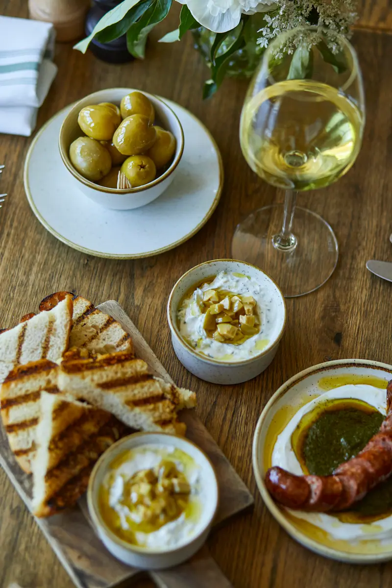 Nibbles to share: green olives, whipped dips, grilled sourdough and a sausage with salsa verde, with white wine