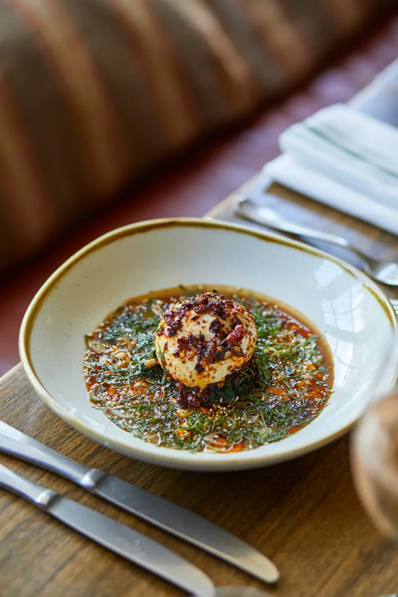 Burrata with a crisp crumb on a vivid green herb dressing, the table laid around it