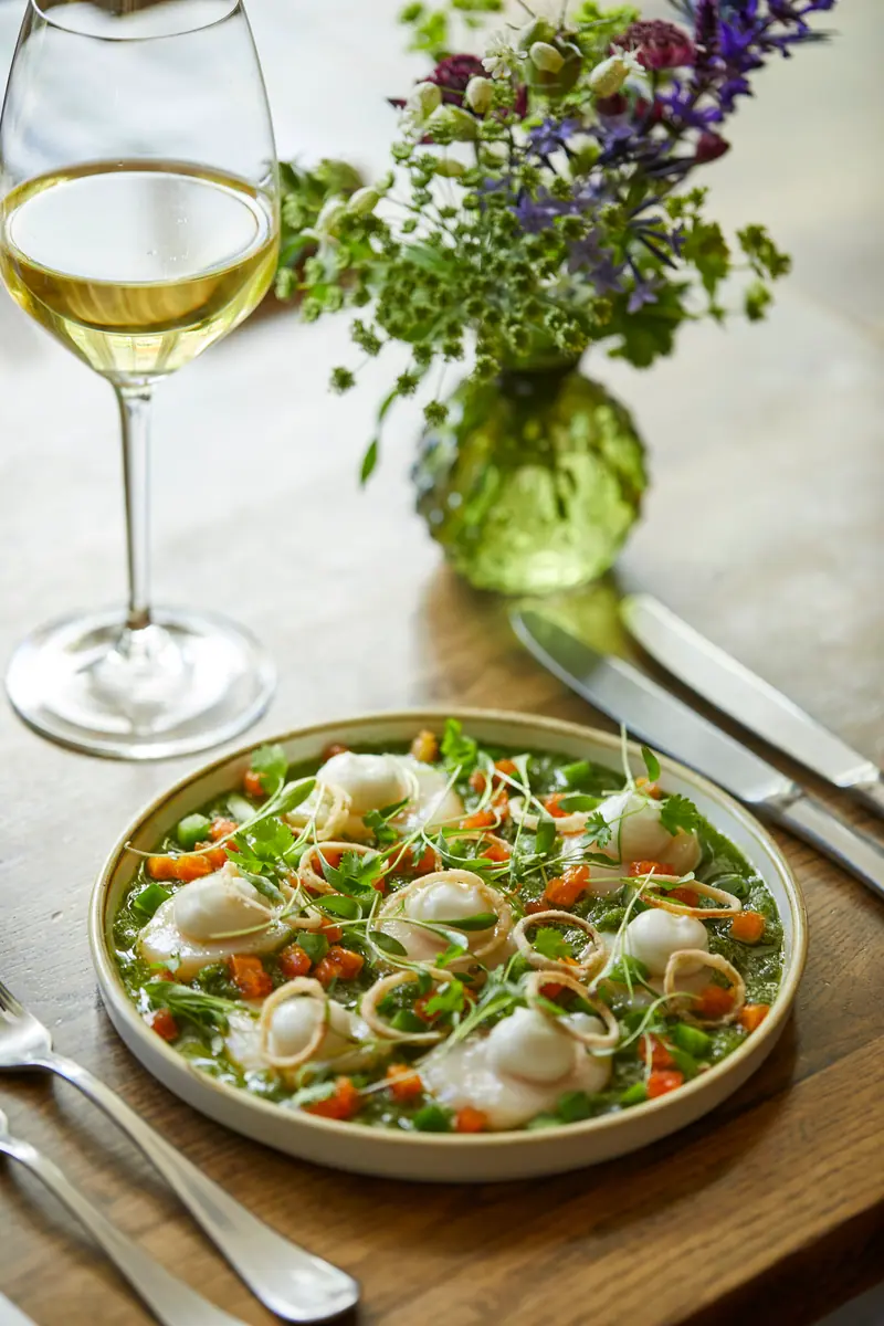 A light summer plate of pea shoots, carrot ribbons and soft curds, with a glass of white wine and wildflowers