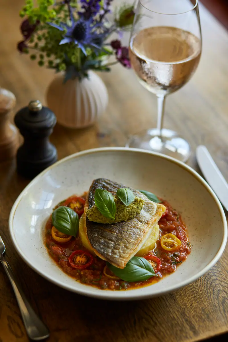 Pan-fried sea bream on a tomato and pepper stew with basil leaves, a glass of rosé behind