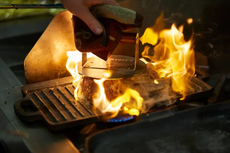 Meat searing over leaping flames on a cast-iron grill in the kitchen