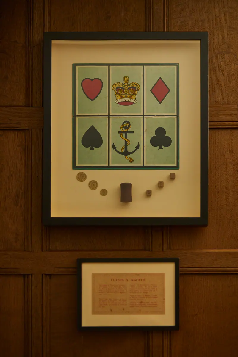 A framed Crown & Anchor board, showing heart, crown, diamond, spade, anchor and club, on the panelled wall