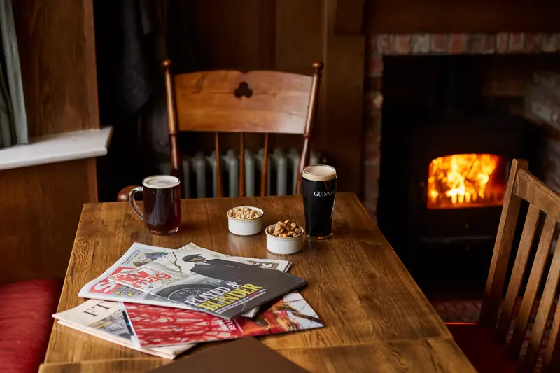 A fireside table with a pint of bitter, a Guinness, bowls of nuts and the weekend papers, the log burner glowing behind