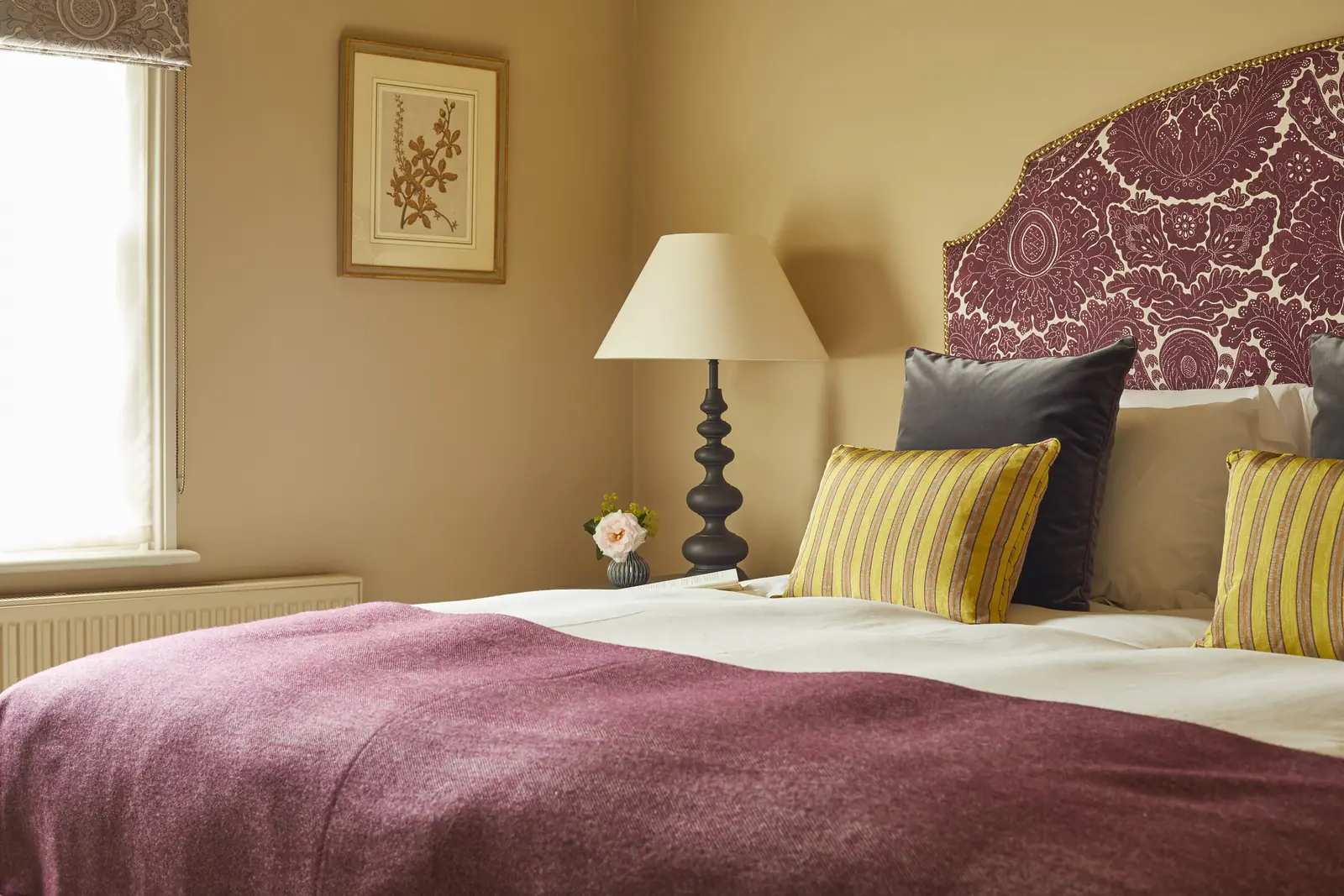 A bedroom with a damask headboard and plum throw